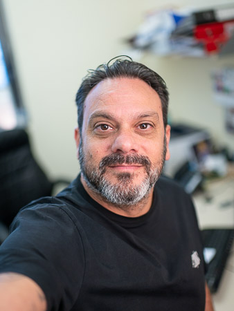 A man in a black shirt is taking a selfie in front of a computer.