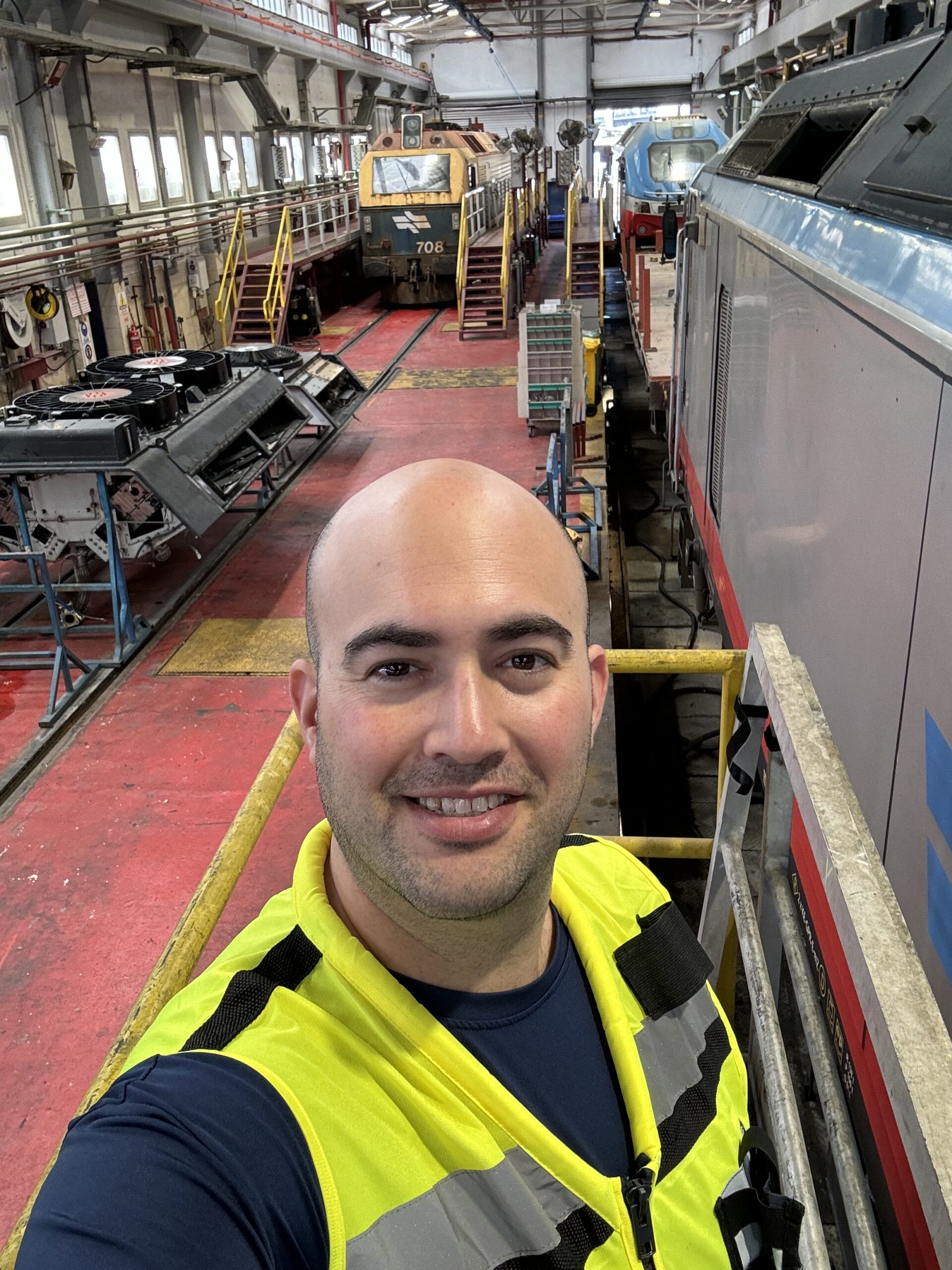 Man in high visibility vest taking a selfie in a train maintenance facility.