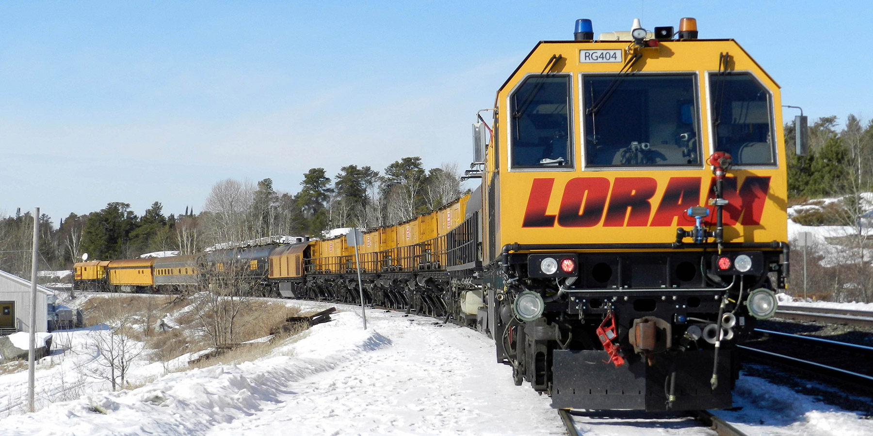Yellow loram rail grinding train on snow-covered tracks on a clear day.