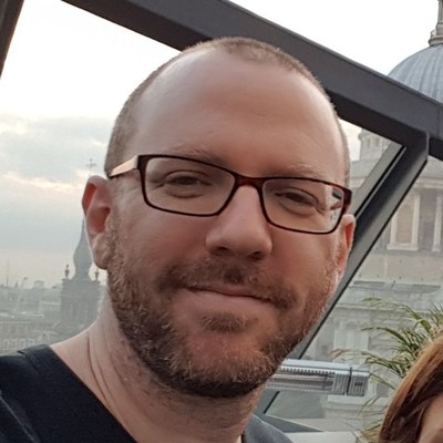 Bearded man wearing glasses seen in front of a building with a dome.